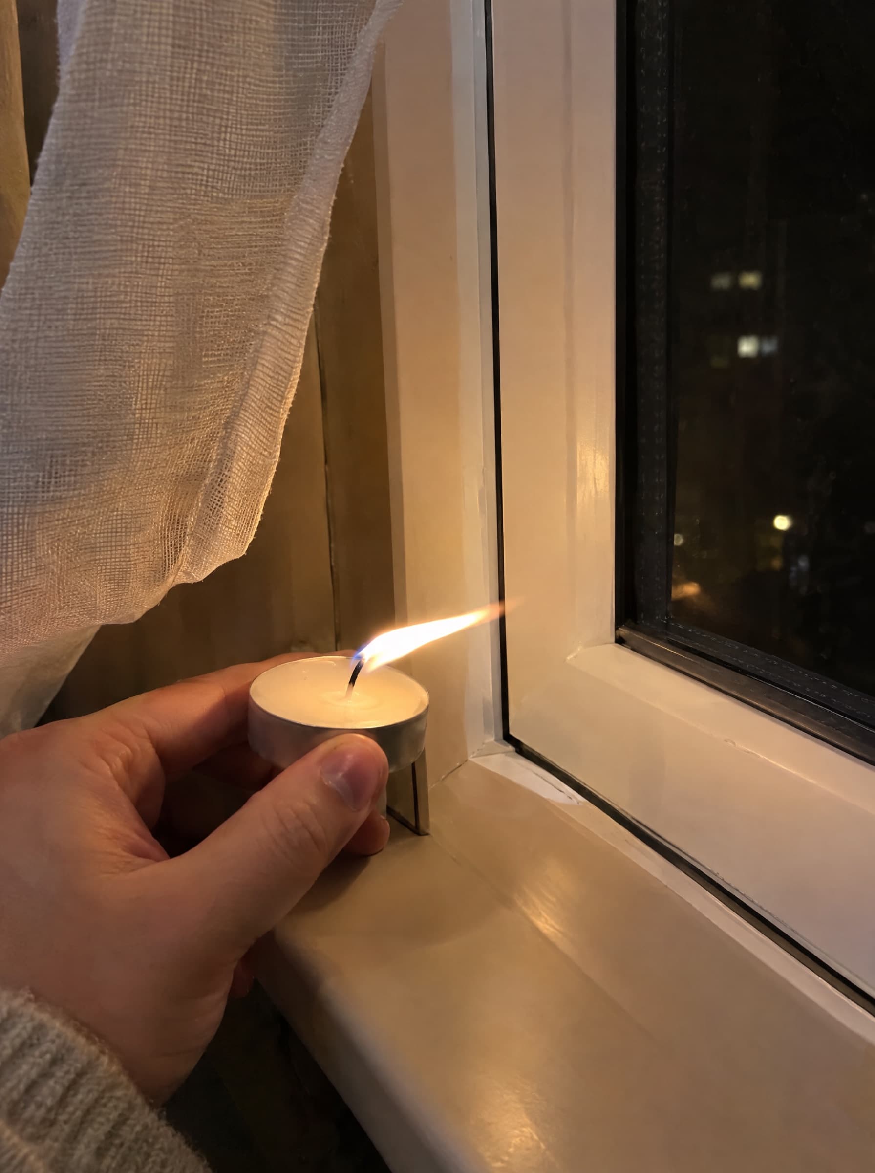 Plamen svíčky se u rámu okna ohýbá průvanem